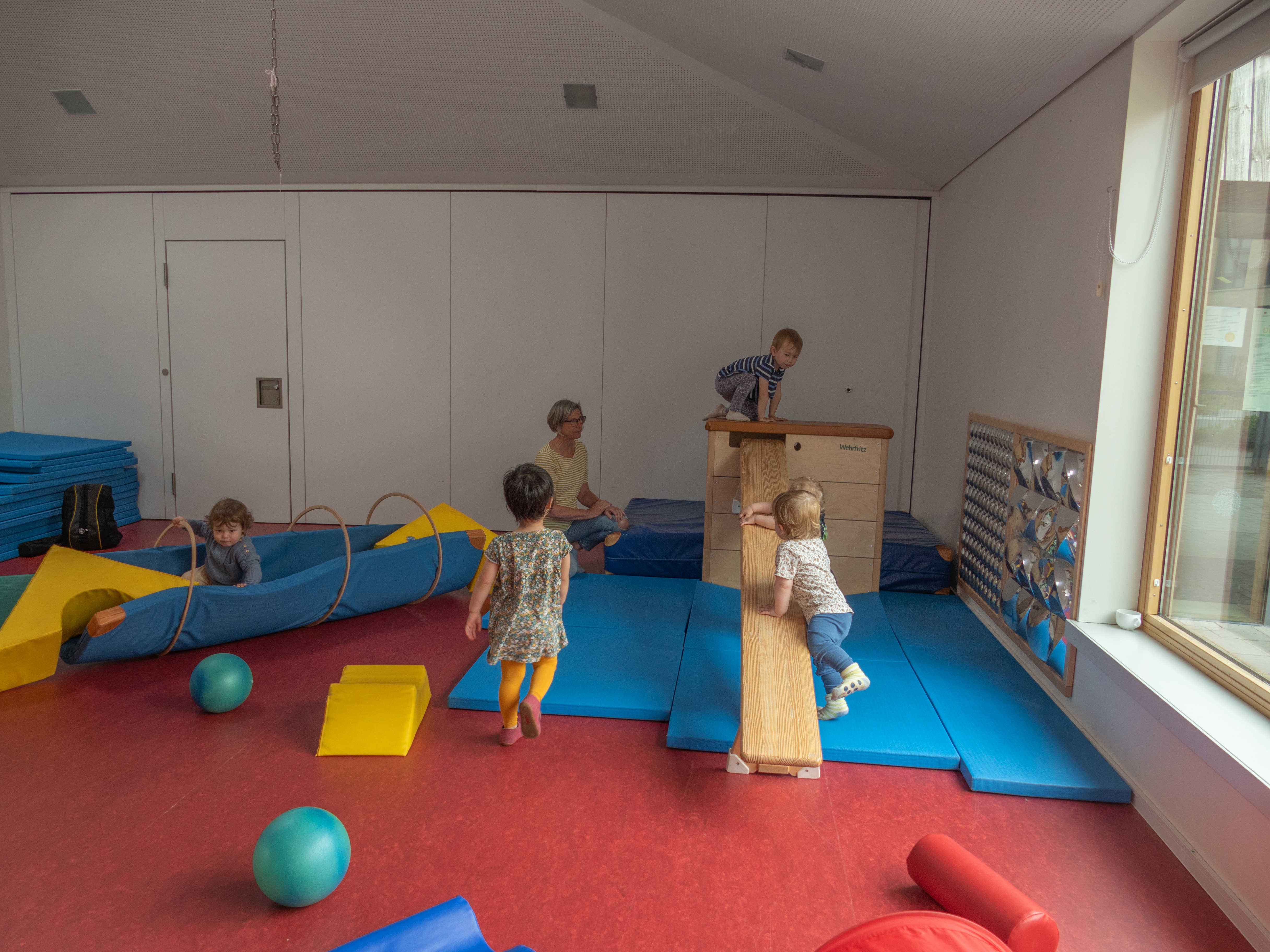 Kinder spielen in einem rieisgen Raum mit Bällen, Spielgeräten aus Schaumstoff und Reifen.