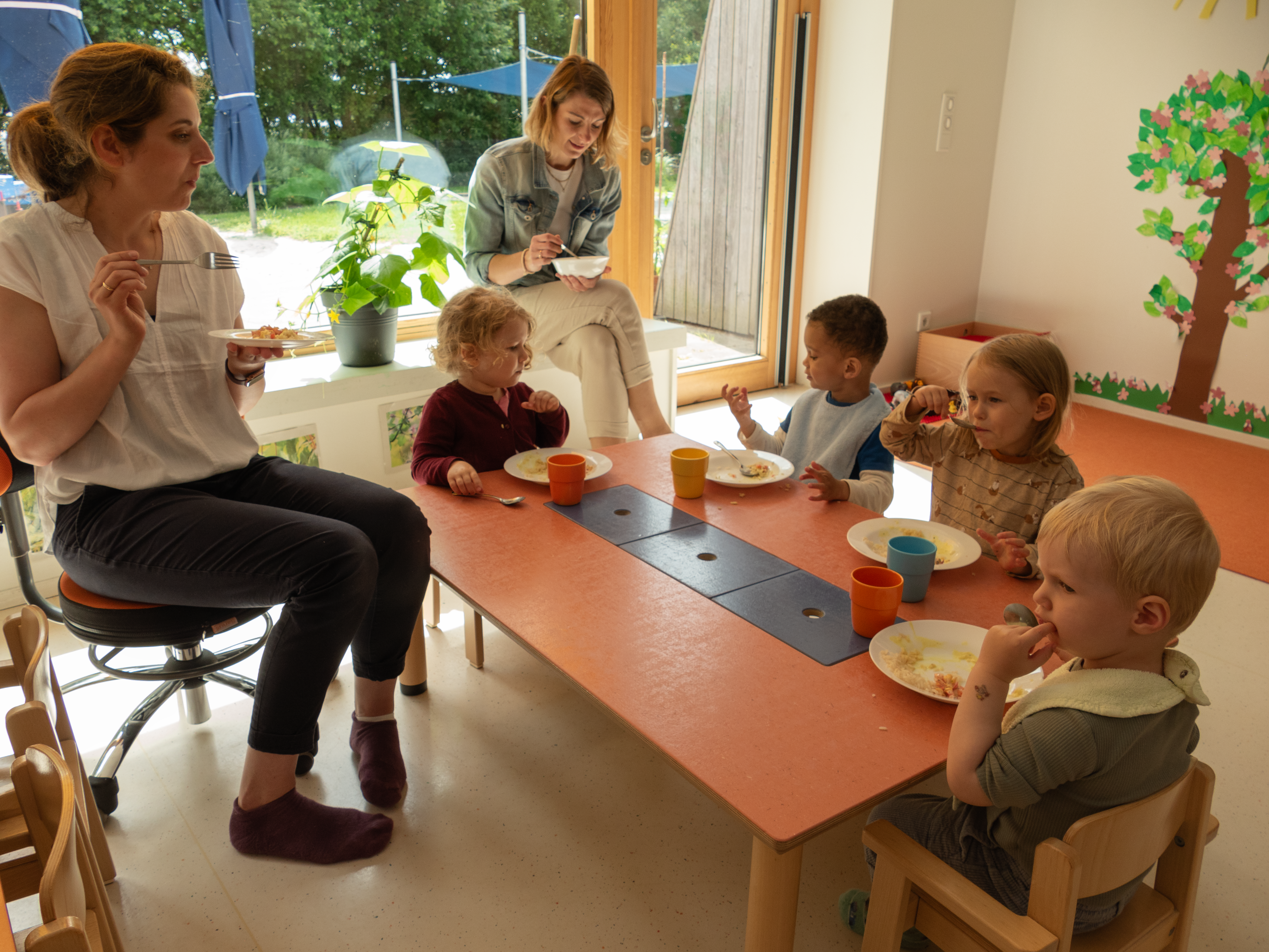 Kindergartenkinder und Erzieherinnen essen miteinander.